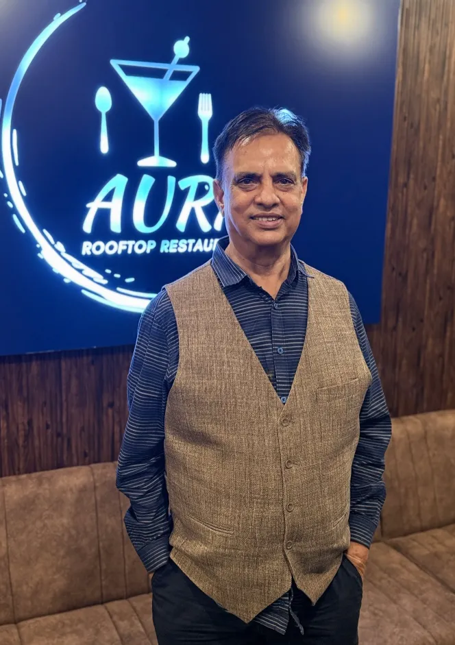 A host standing in front of the Aura Rooftop neon sign